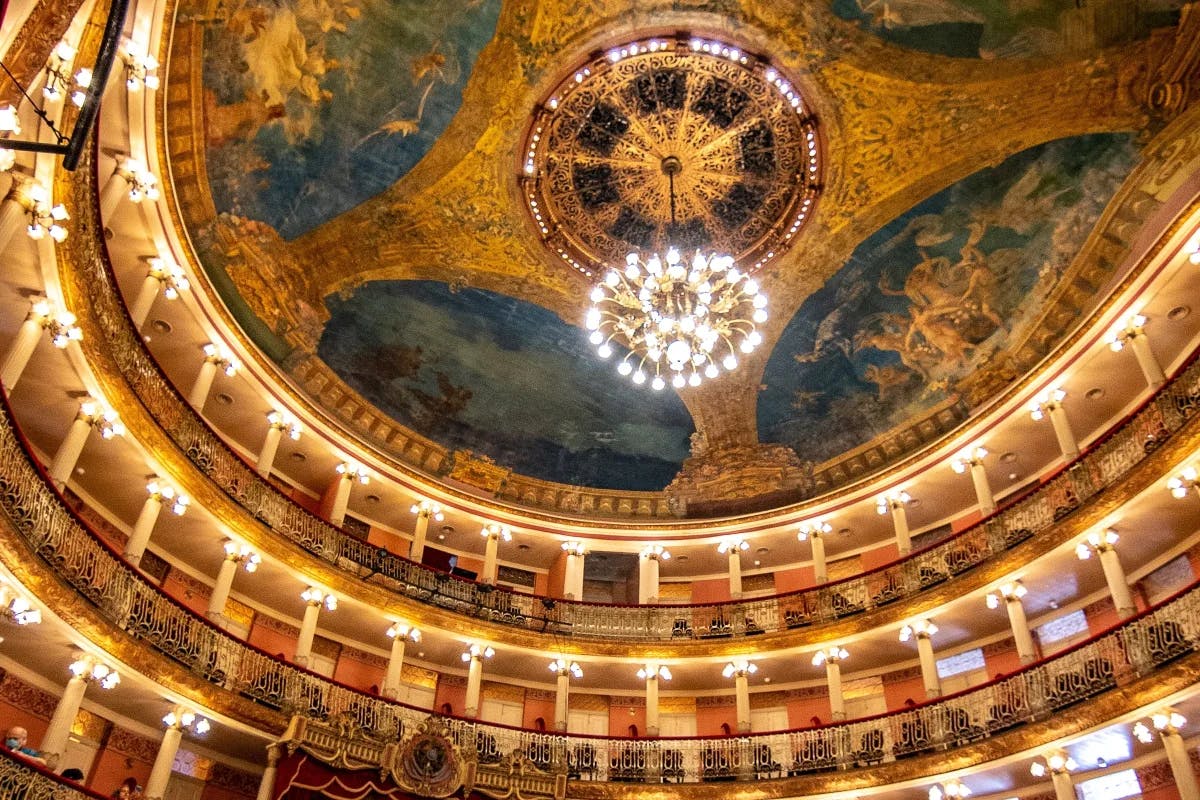 A large ornate ceiling with a chandelier can be seen at Teatro Amazonas.