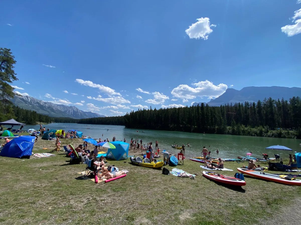 A lake with people chilling on its bank with their kayaks and umbrellas. 