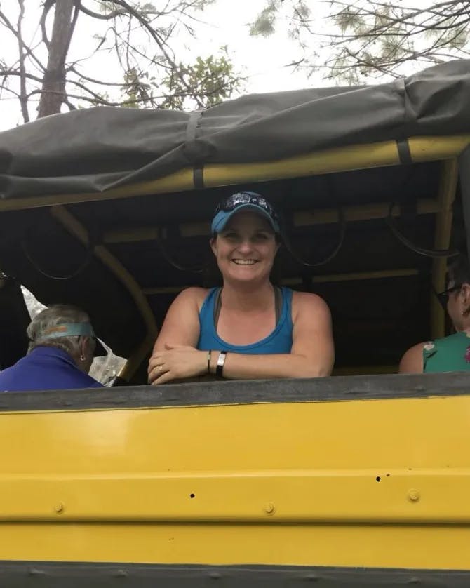Katie wearing a baseball cap and blue tank top on the back of a yellow bus