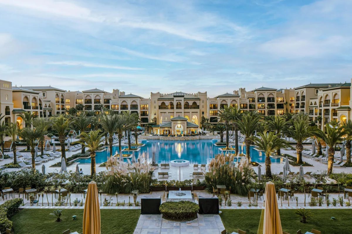 aerial view of a luxe Moroccan resort centered on a big pool surrounded by palm trees