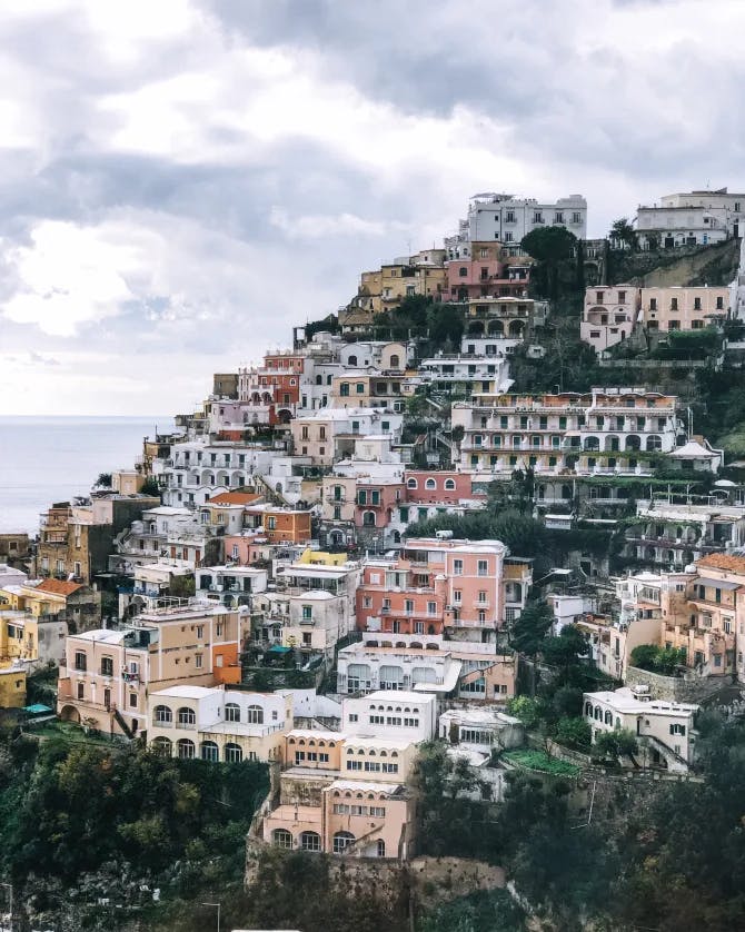 Picture of an Italian coast with colorful houses layered on a cliff and a cloudy sky in the background