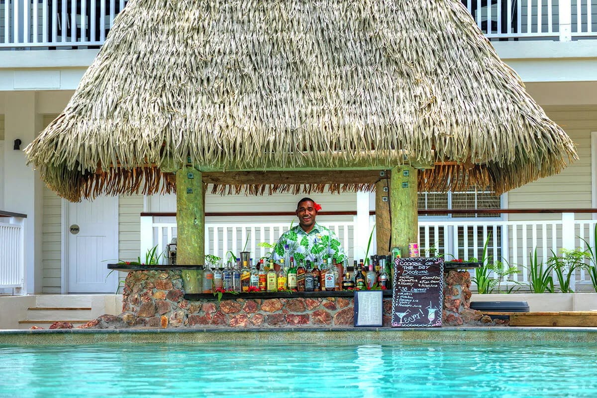 A juice shop at the beach with a man standing in it on a sunny day.