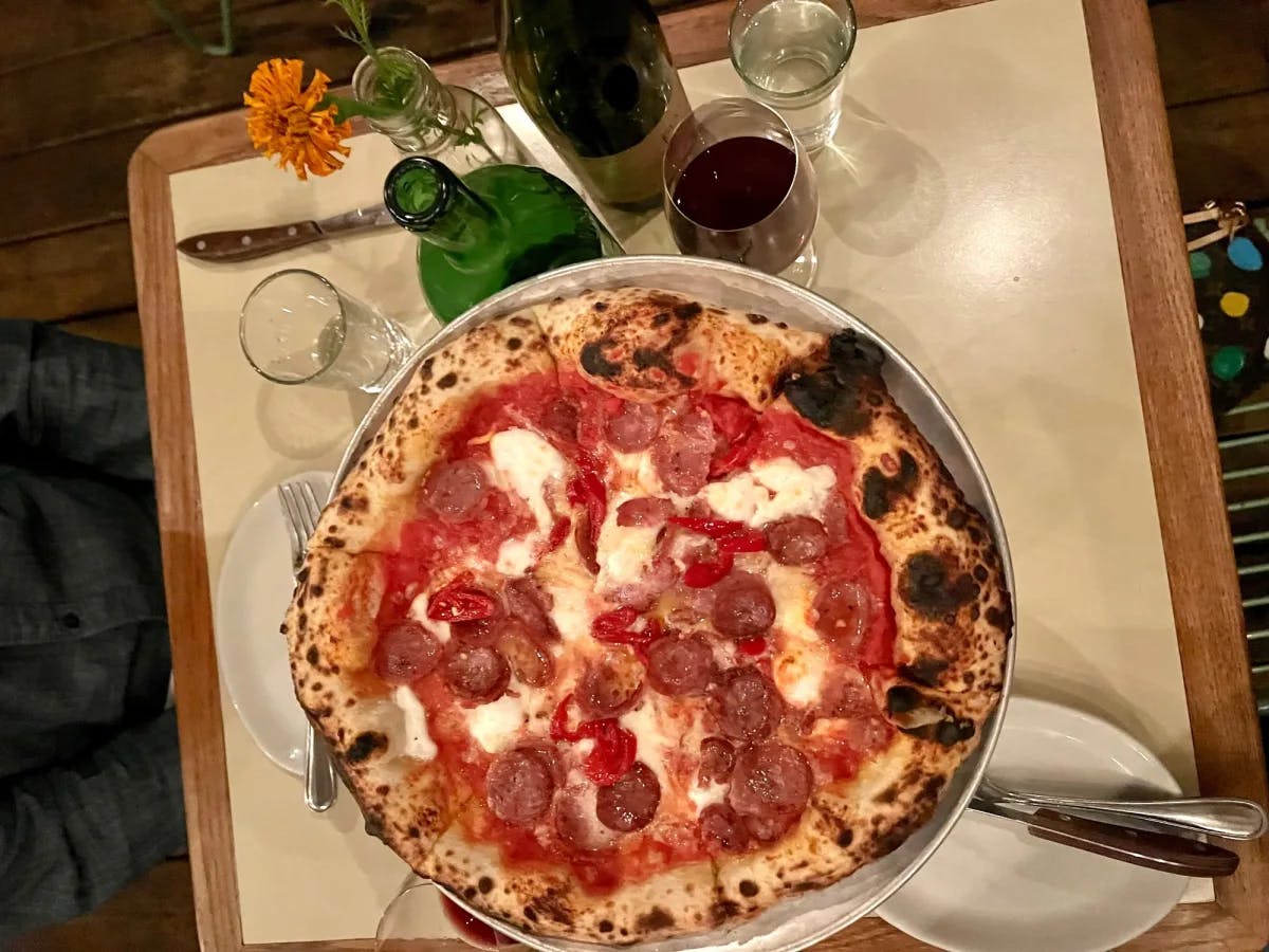 Pepperoni pizza on a table with drinks and serving plates. 