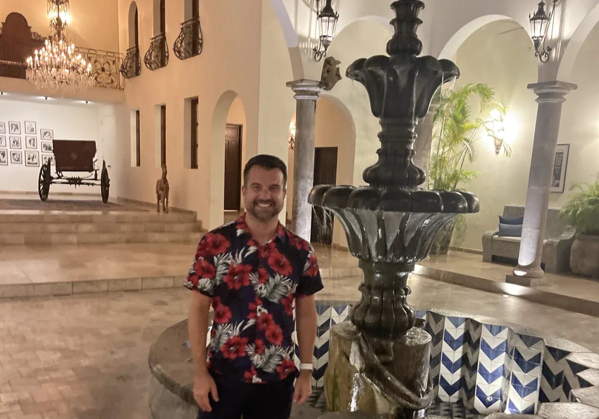 Travel advisor Eric standing in front of a fountain at an elegant residence with pillars and arches and a chandelier in view