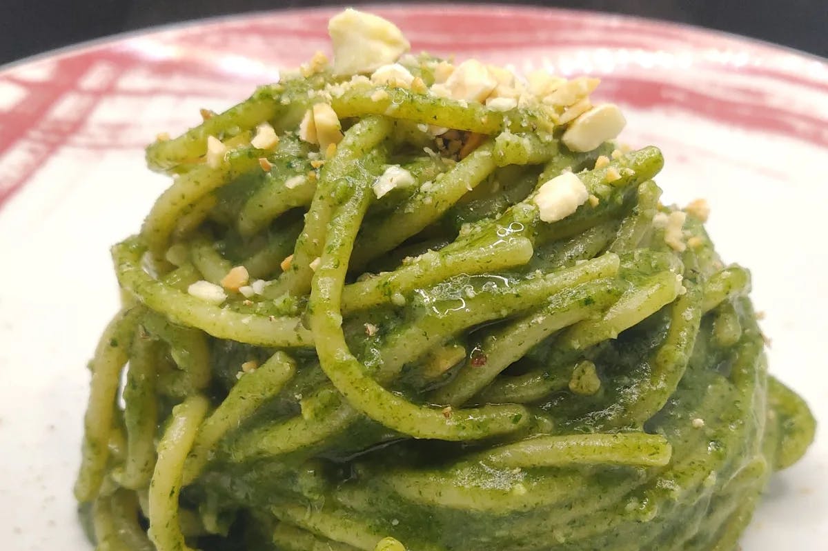 white plate with pesto pasta and a garnish 