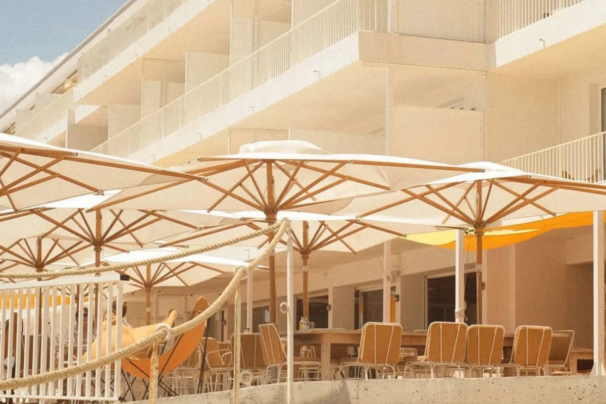 outdoor terrace with tables and white umbrellas outside a white hotel