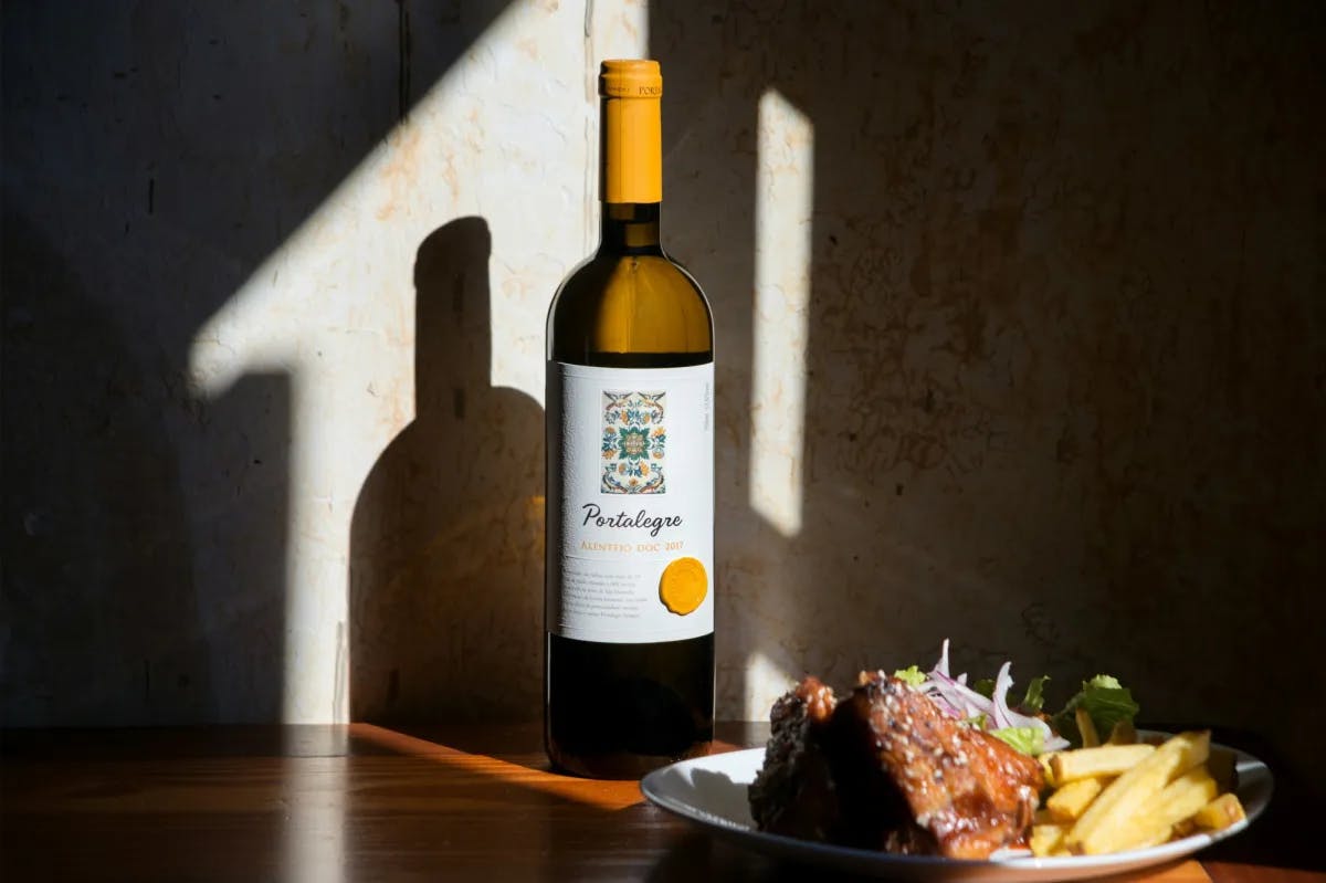 Wine bottle with a plate of food on table.