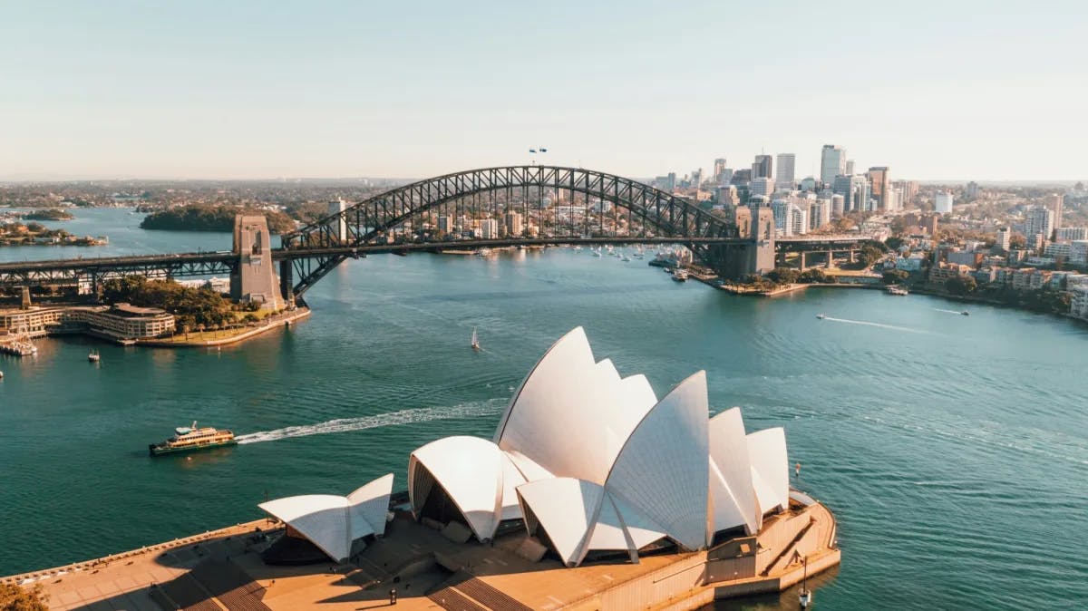 Aerial view of an arched bridge over a body of water and a white petal shaped building during daytime, also known as the Sydney Opera House.