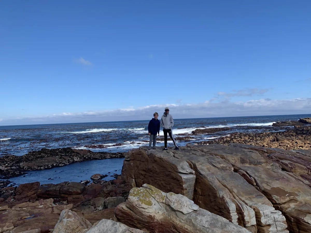 Two people standing on a rock at a beach during the daytime