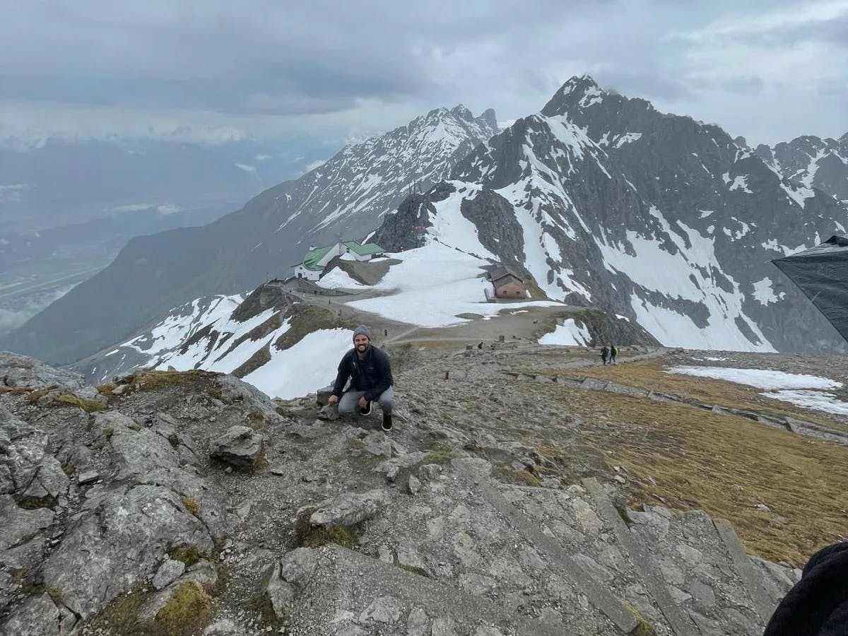 A man perched on a path leading to a snowy mountain peak. 