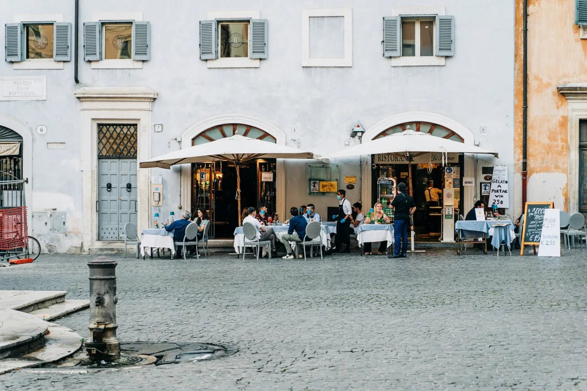 Picture of people dining at a quaint outdoor restaurant in a street in Rome with white umbrellas 