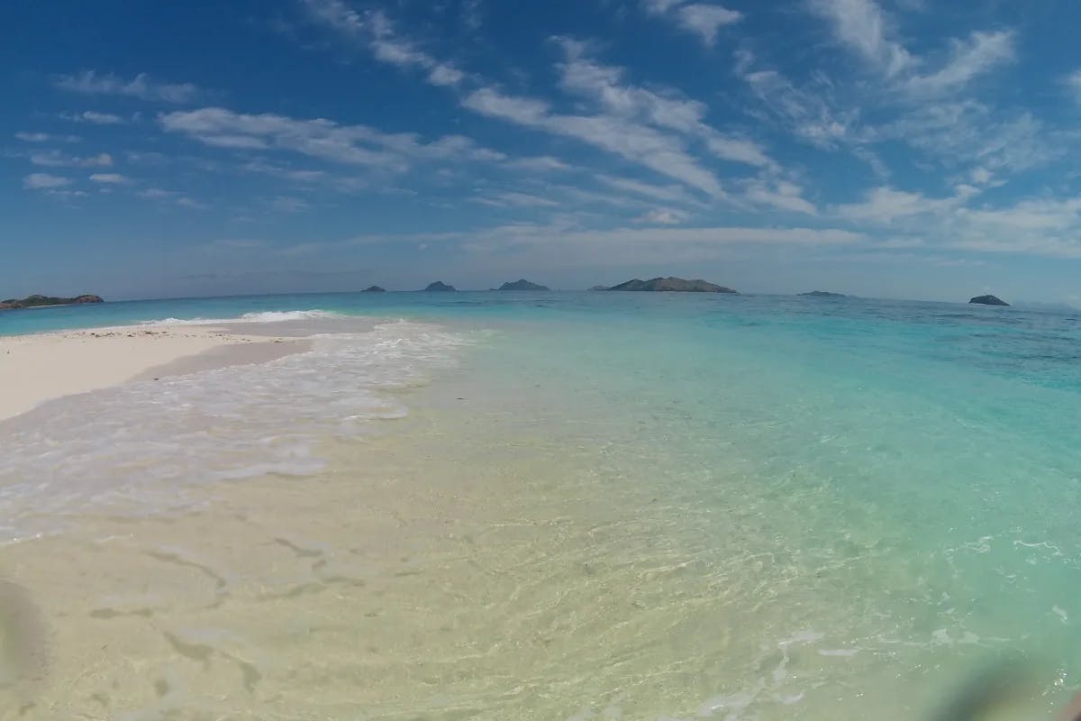 A picture of the beach during the daytime with crystal clear blue water beneath blue skies.