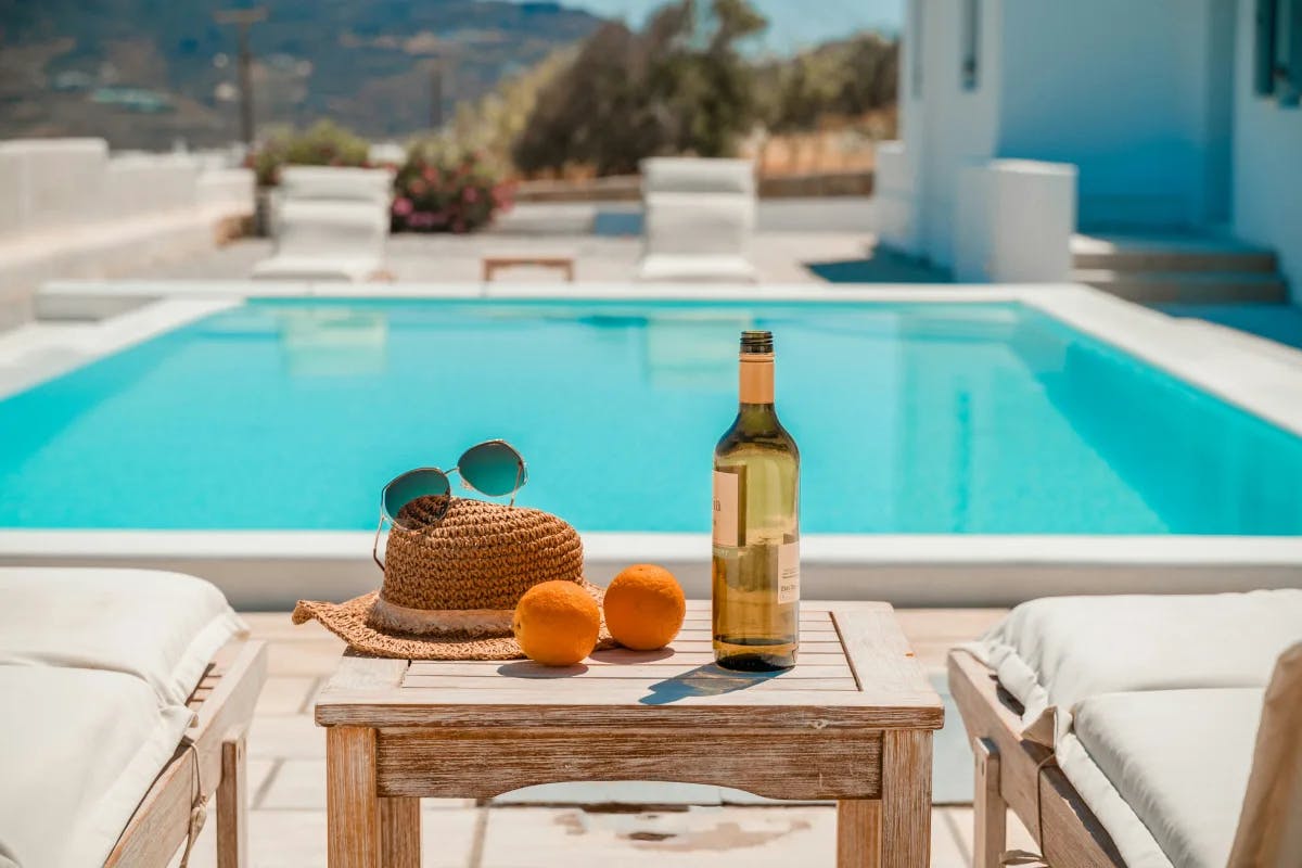 A picture of a bottle and orange placed on a table near a swimming pool.