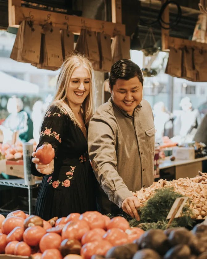 A photo of two people shopping for tomatoes at a food market 