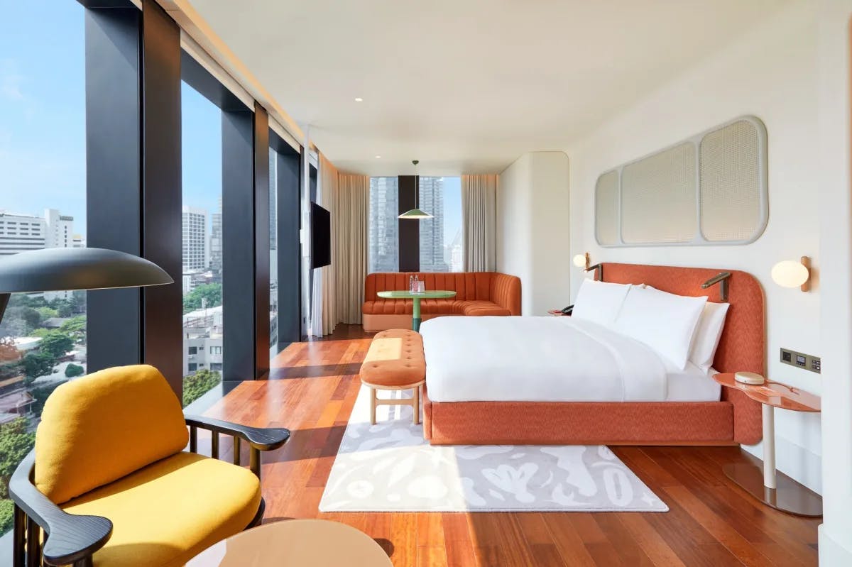 a modern hotel room on a high floor in a tall tower with a yellow chair, wooden floors, and an orange bed frame