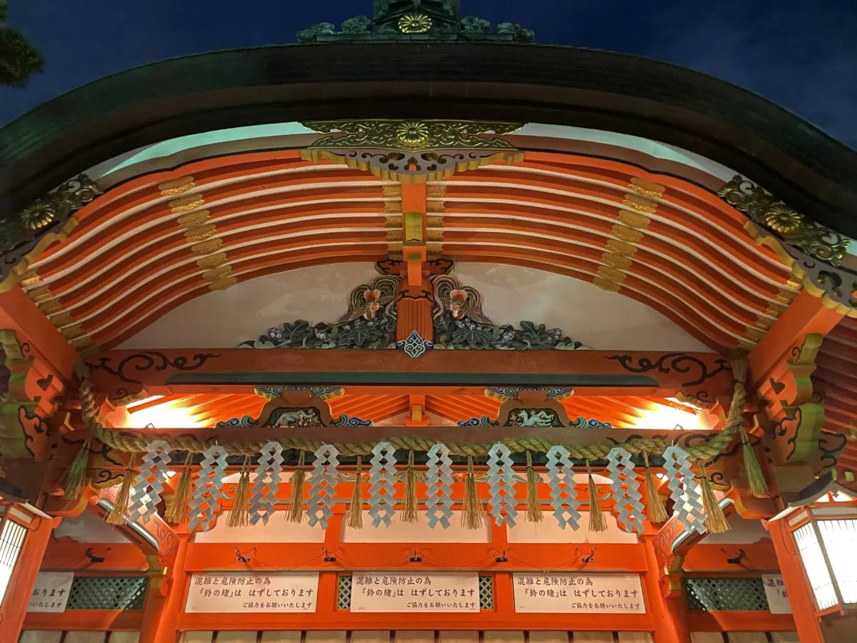 The image shows the intricately decorated underside of a traditional Japanese structure at dusk, highlighting its architectural beauty.