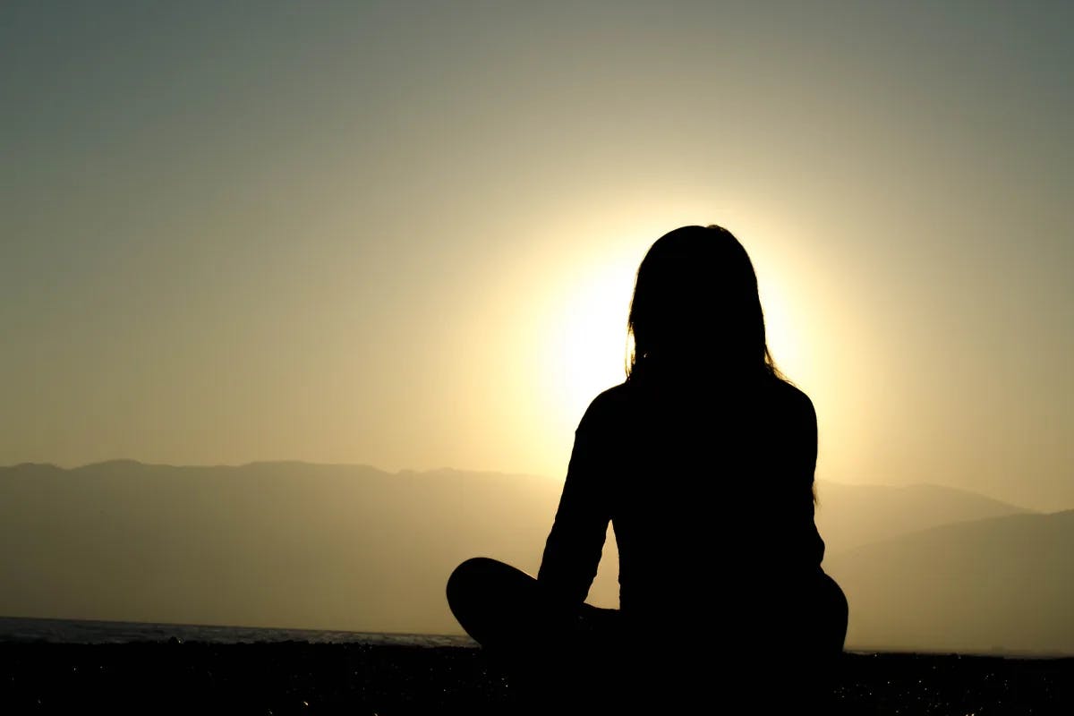 A picture of a girl meditating at the sunrise.
