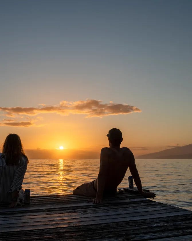 Couple sitting beside sea under sunset