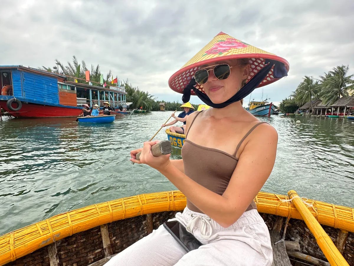 Isabel in a traditional pointed straw hat on a round basket boat on a river.