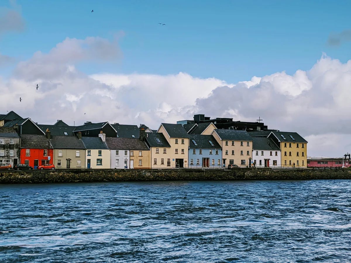 Colorful houses along the water in Galway on a sunny day with clouds.