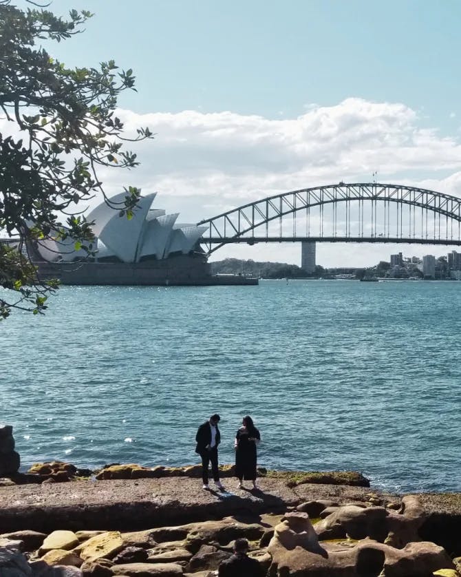 iconic bridge over water and two people standing on a rocky shore