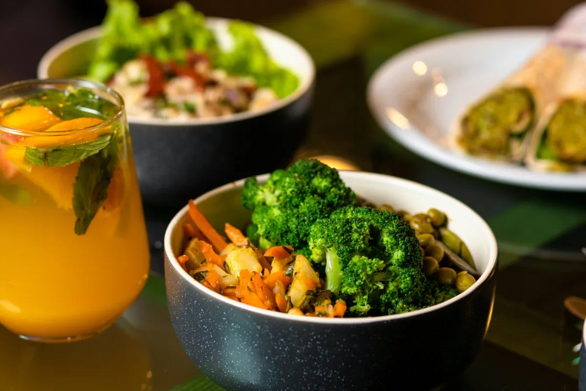 A picture of green vegetables served on white ceramic bowls with a glass of juice at a restaurant.