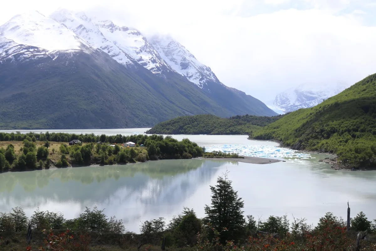 Lake view with snow covered mountains and green fields. 