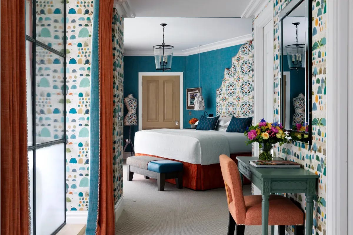 a luxe hotel room with blue walls and a bed with an oversized upholstered headboard covered in boldly patterned fabric