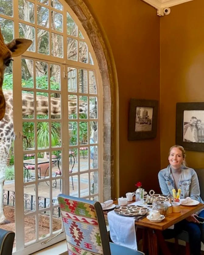 Picture of Lori sitting in a resturant with giraffe peeking inside