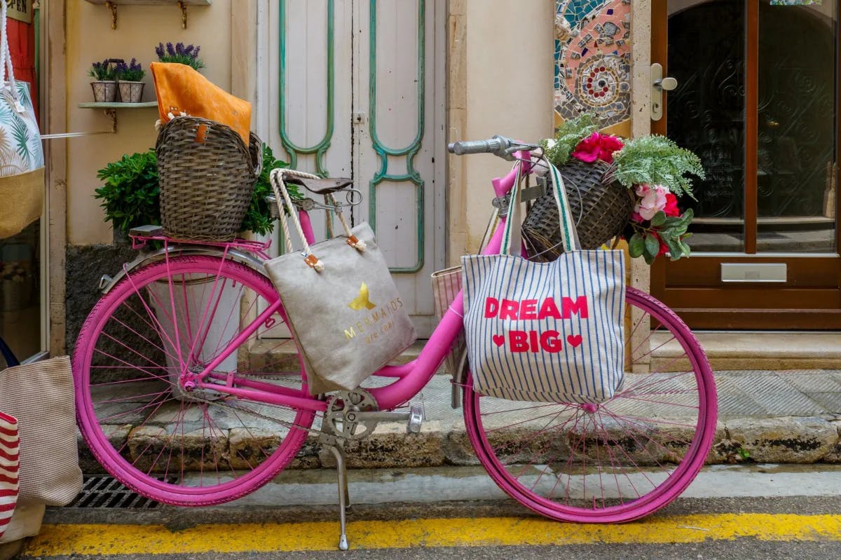 Pink bicycle with bags, baskets and flowers parked in front of a house. 