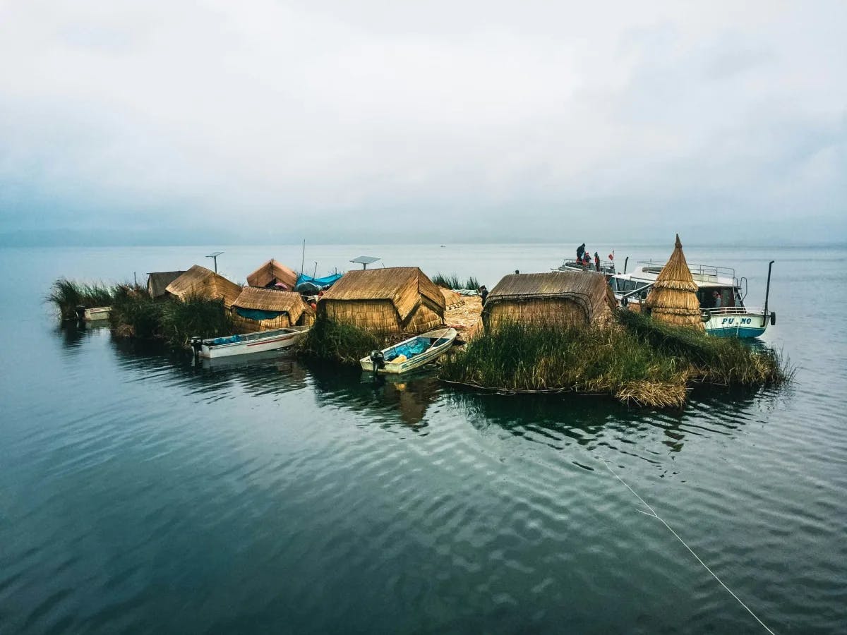 A look at the Uros Islands, made from totora reeds, including some small shacks and boats on a sunny day.