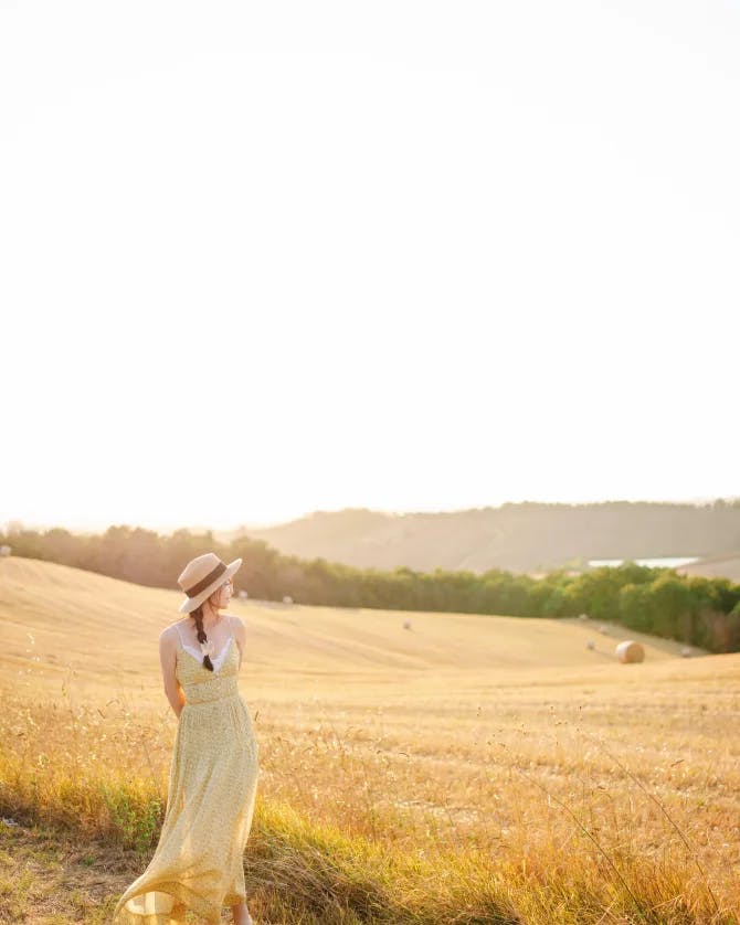 Advisor in a dress posing by a large grassy hill area the the sunlight 