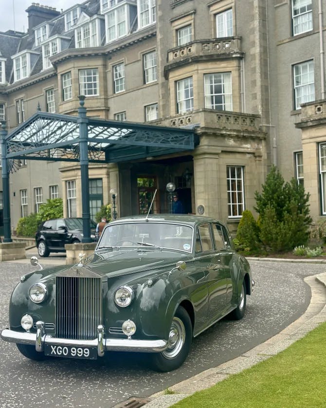 View of an old-fashioned green car parked in front of the entrance to a grand hotel