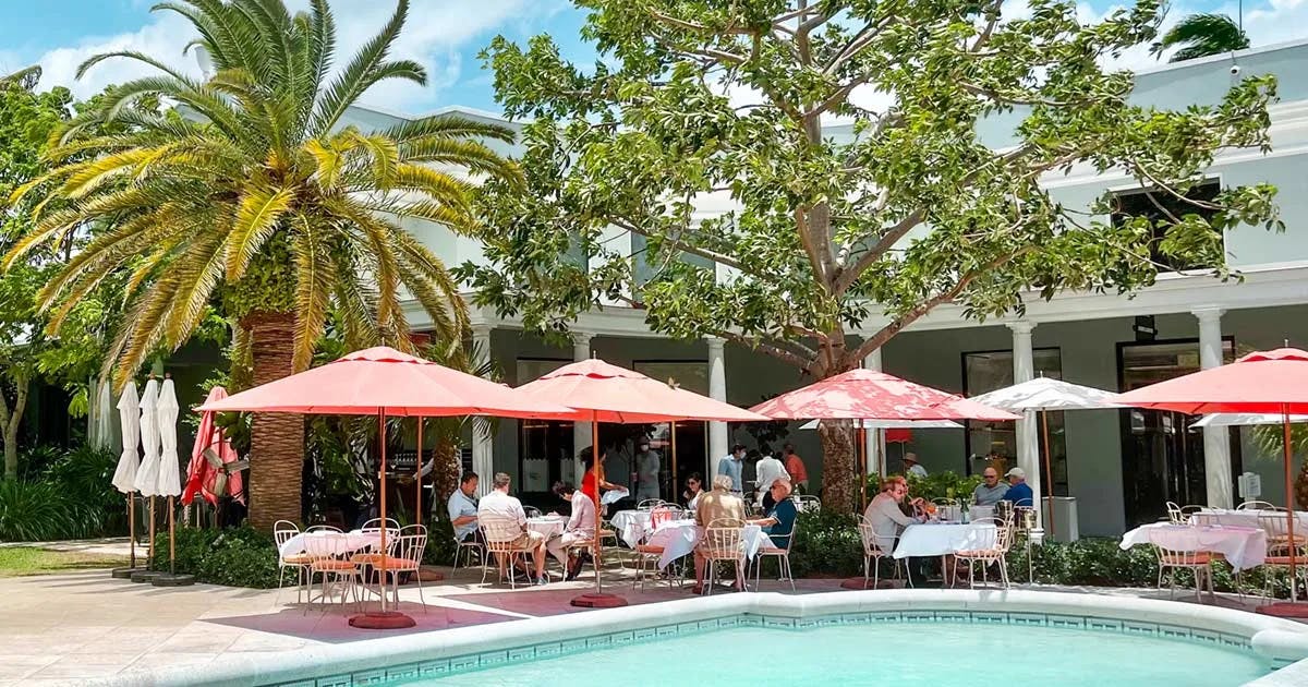 A view of a pool at a shopping center with plam trees and lovely sun umbrellas. 