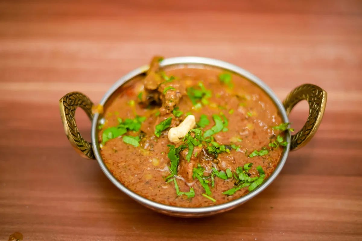 A silver dish with curry on a wooden table.