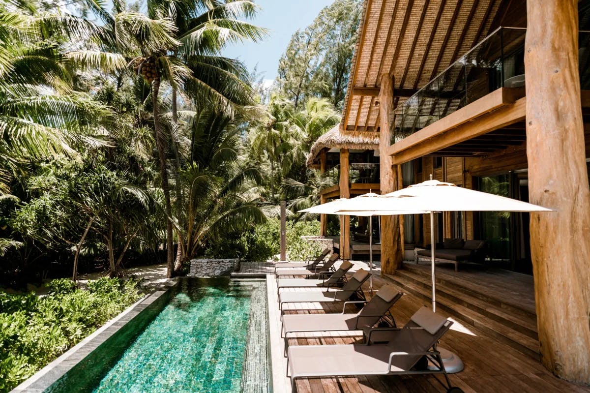 a luxury wooden home in the jungle with a broad porch overlooking a luxe pool 