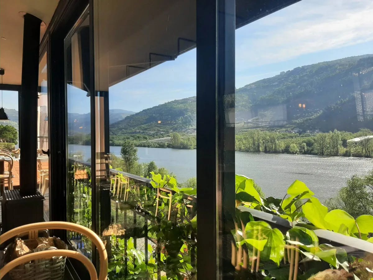 An indoor restaurant with a view of a valley with a lake flowing through it 