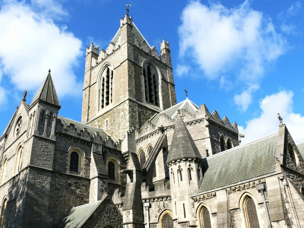 The image depicts a large, historic stone church with pointed arches and a prominent tower set against a blue sky with clouds.