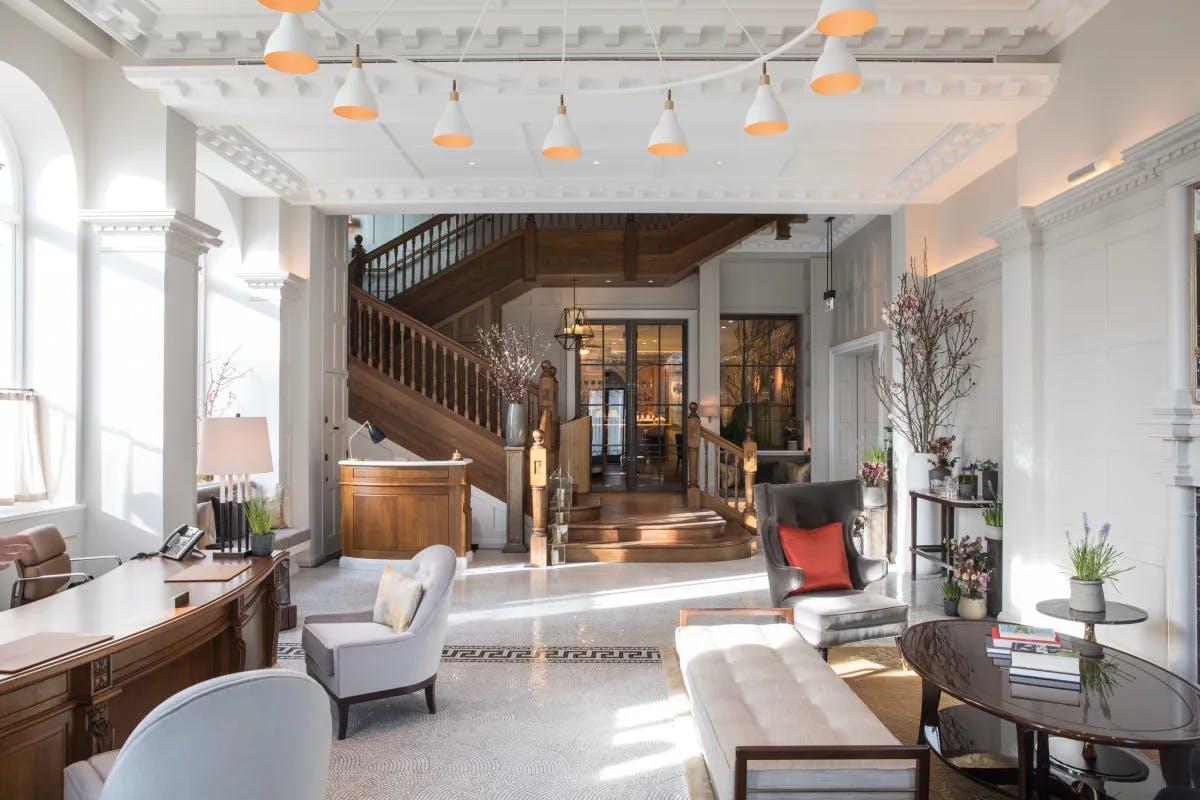 Spacious white lobby with modern furnishings leading to classic wooden staircase in the Cadogan London.