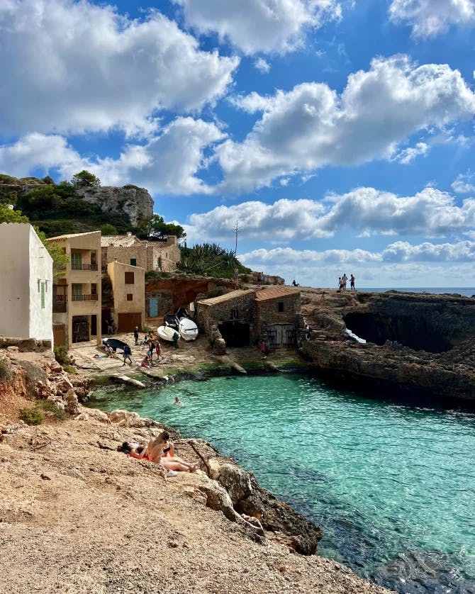 Small intimate beach, with clear, azure water next to small, stone houses.