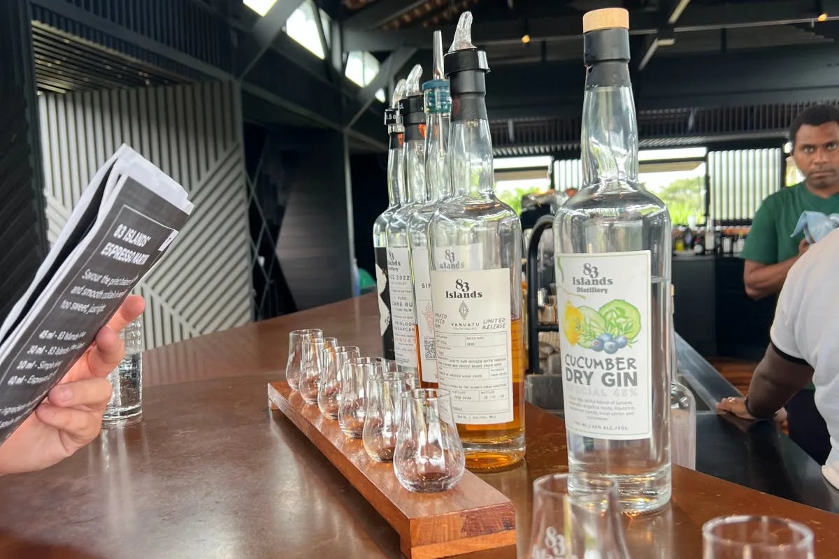 A row of small glasses lined up inside of a wooden board with the same number of liquor bottles standing next to them on the bar, ready for a liquor tasting.