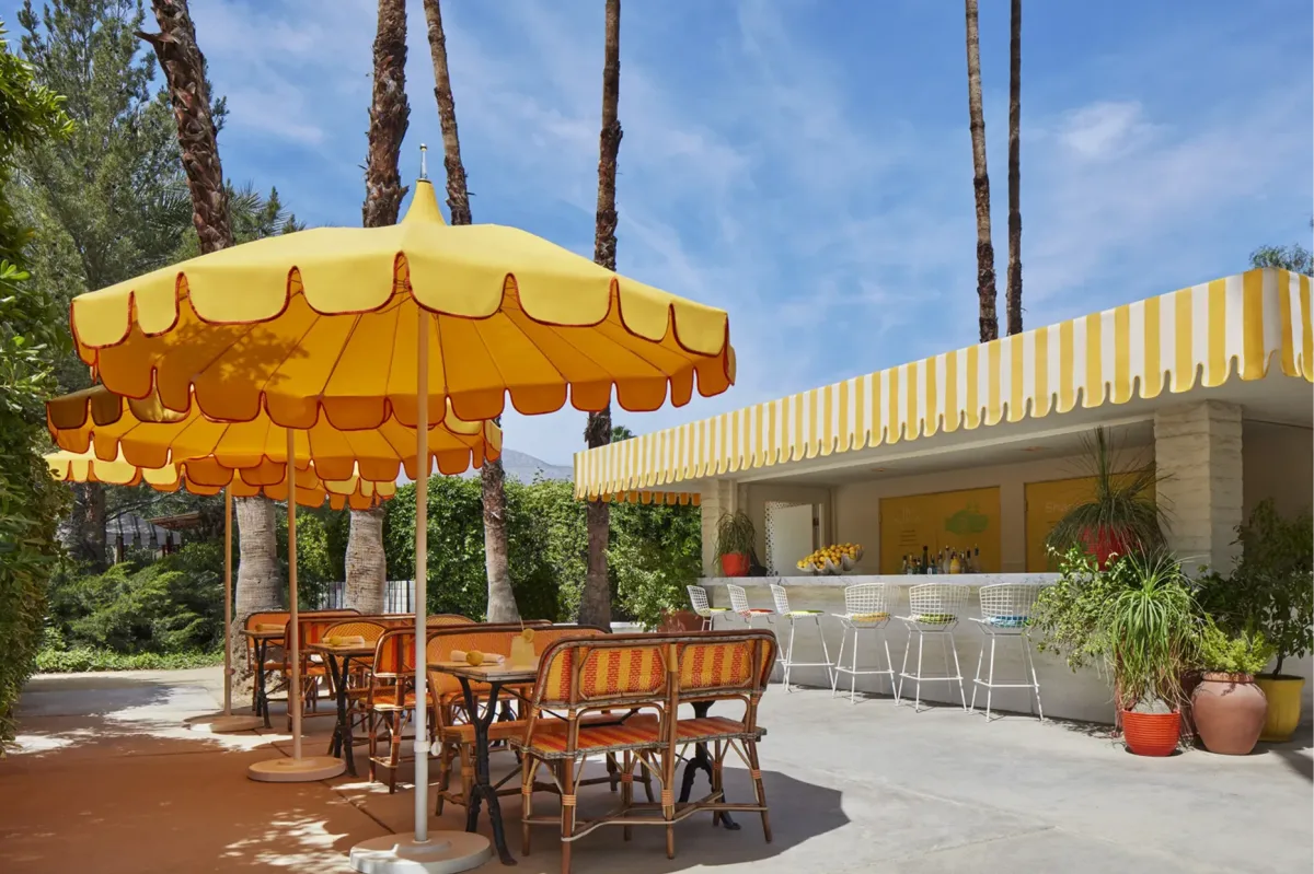 a sunny courtyard with yellow umbrellas and a charming lemonade shack