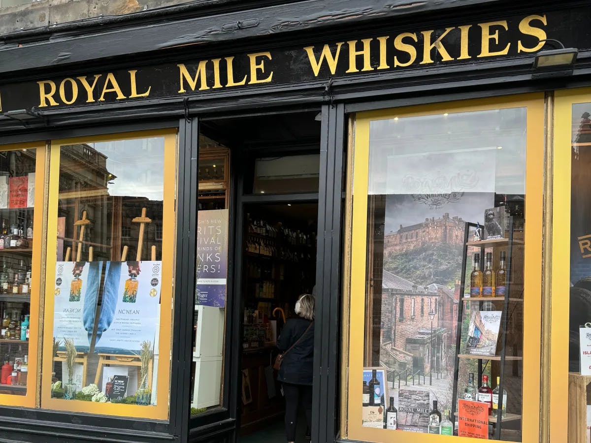 The exterior of “ROYAL MILE WHISKIES,” a whisky store with a black and yellow facade, large display windows, and an open entrance revealing a glimpse of the interior.