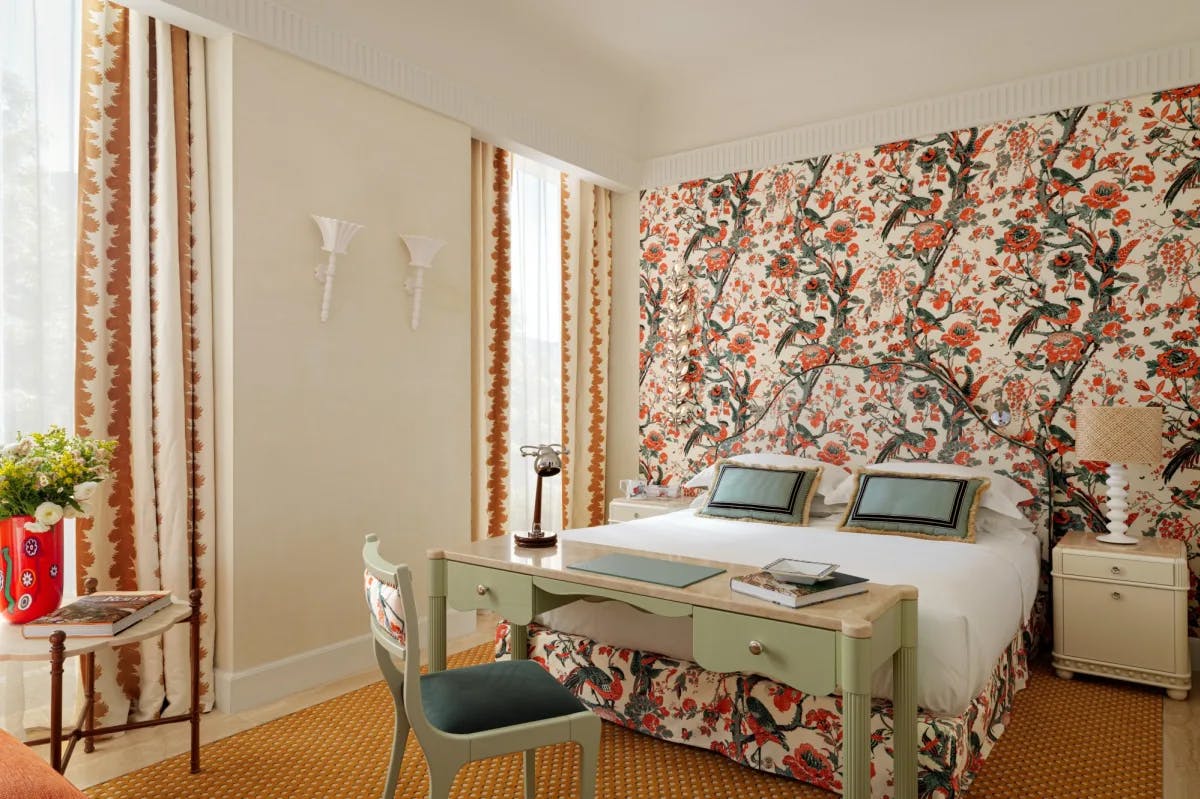 a vibrant hotel room with floral wallpaper and an artistically funky red vase filled with flowers