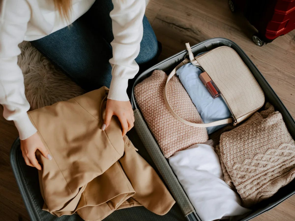 An open suitcase is being packed with neatly folded clothes and a travel document, suggesting preparation for a trip.