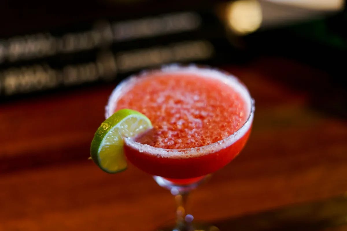 A red, frozen alcoholic beverage, with a salt-coated rim and topped with a lime wedge. 