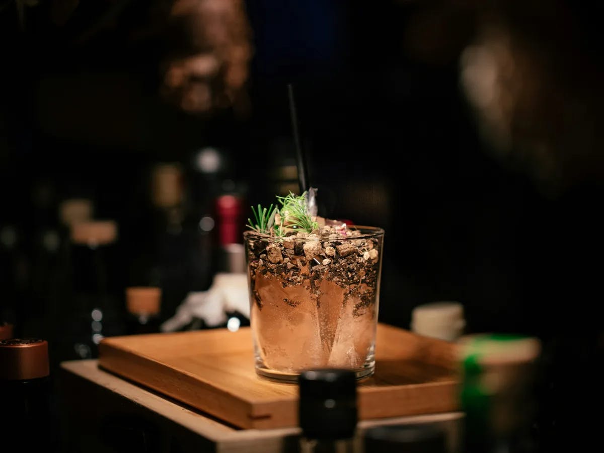 A cocktail garnished with herbs, poised on a wooden surface.