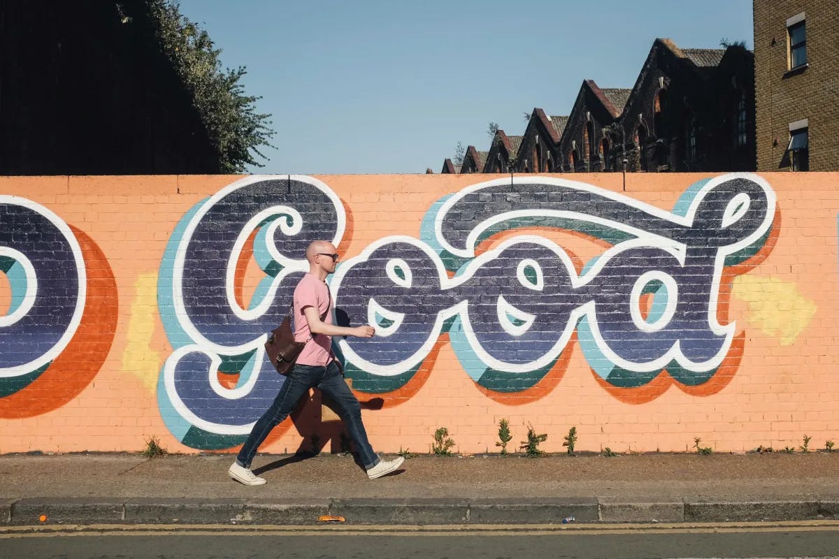 Man walking next to a graffitied wall that says "good" on the last day of a London 4–day itinerary.