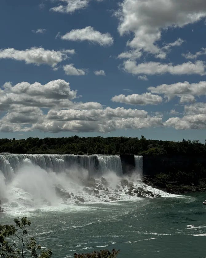 View of a very large waterfall pouring into a body of water surrounded by hills on a sunny day