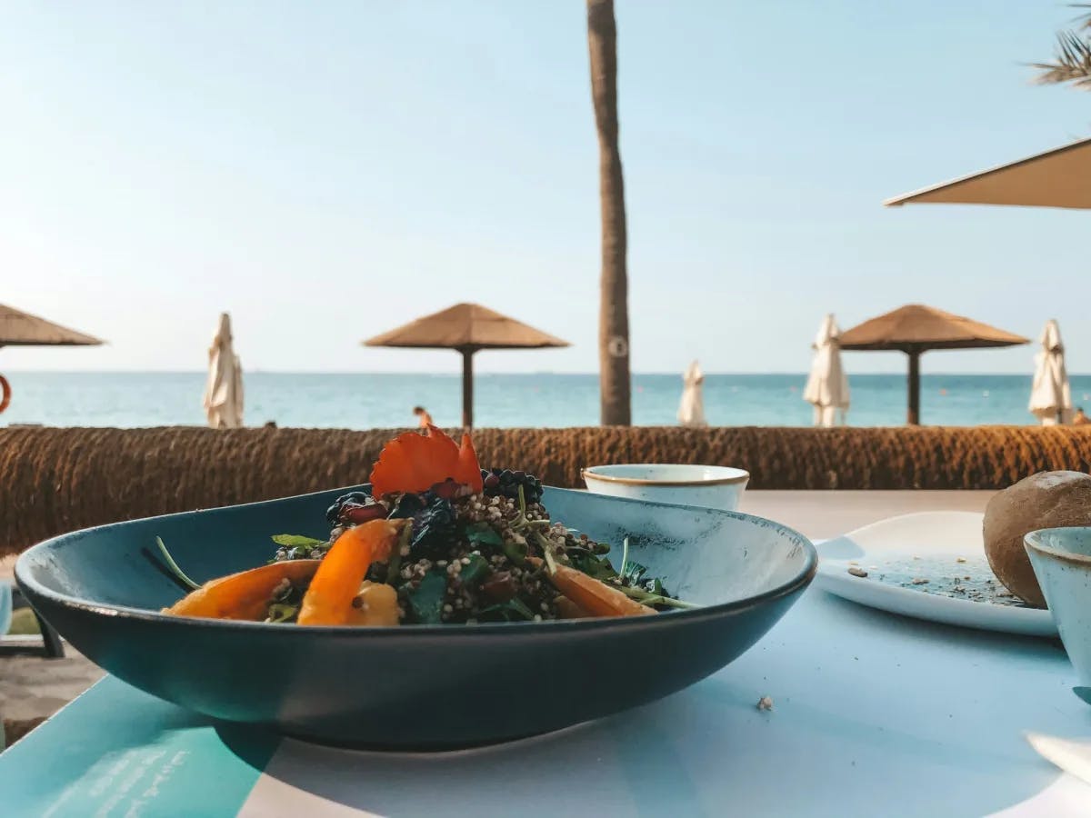 Food in a black bowl on a table in front of beach.